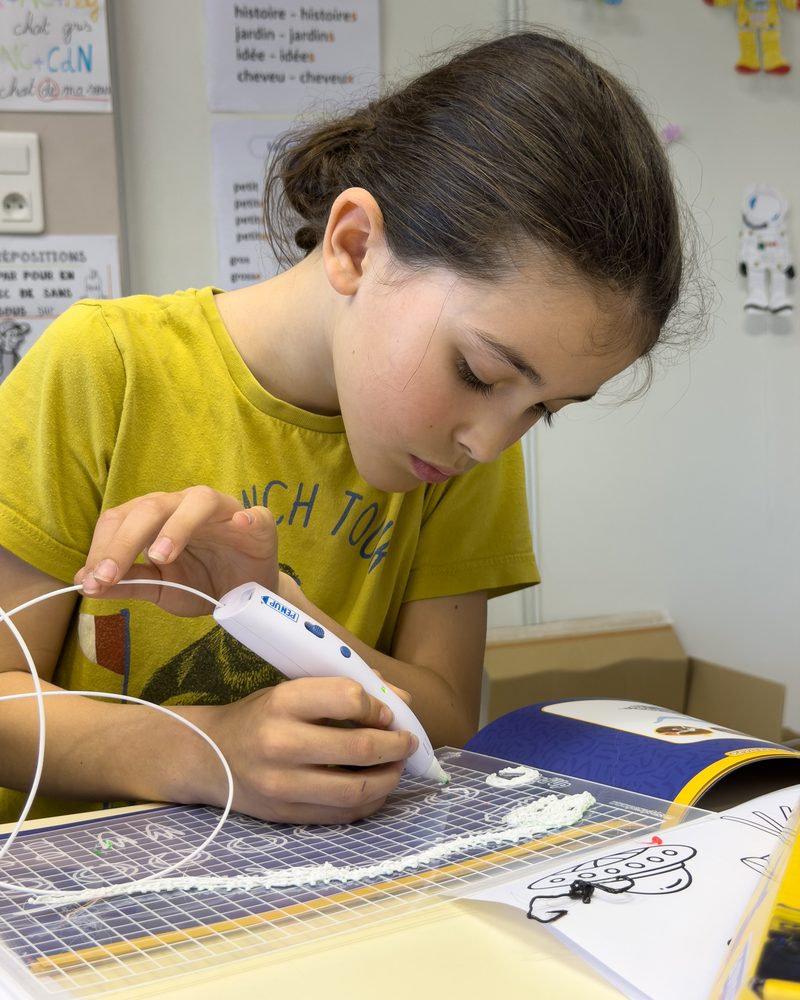 Une enfant trace sa première forme au stylo 3D sur un tapis à pochoirs