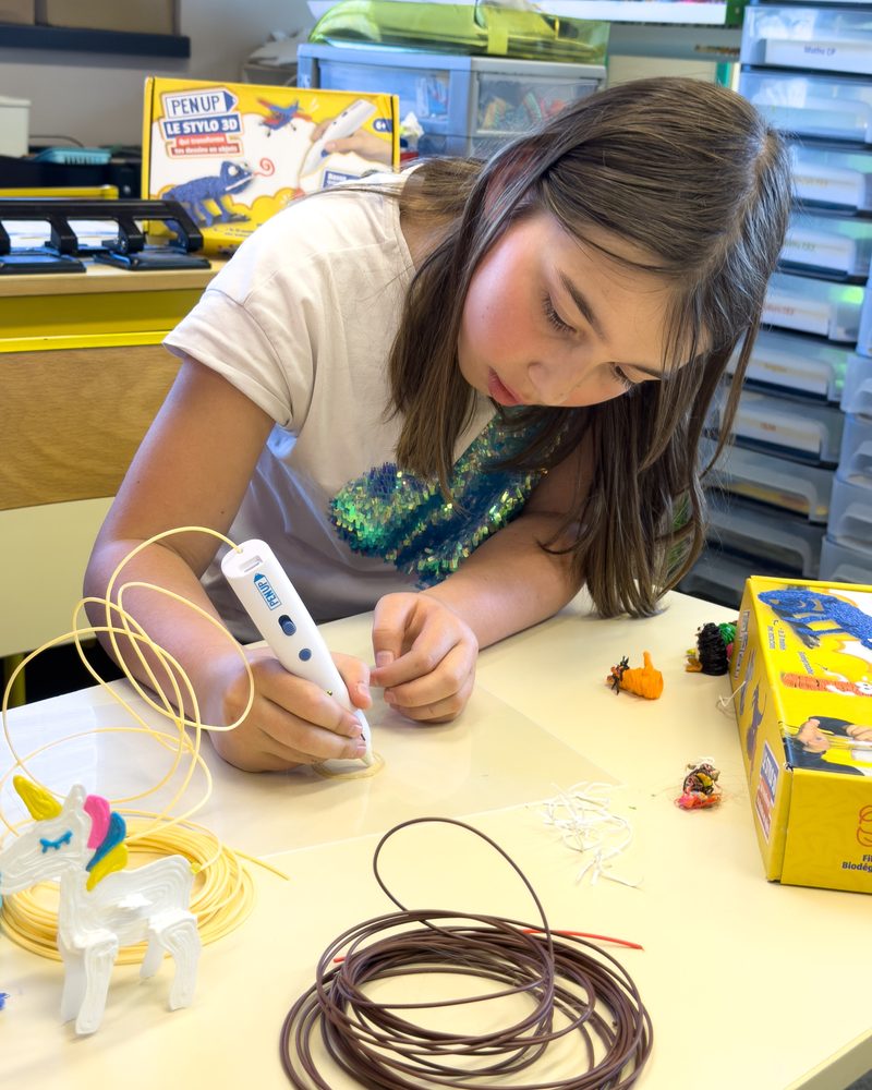 Une enfant vérifie le filament de son stylo 3D posé sur la table