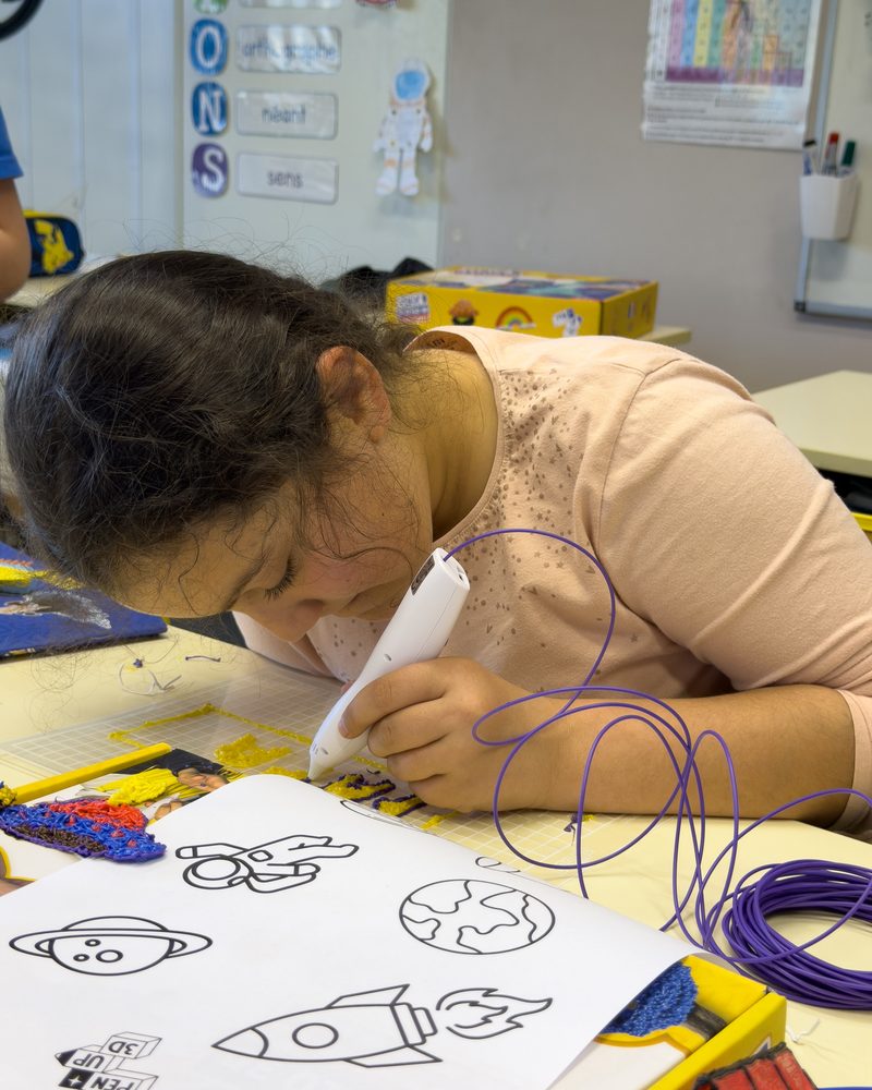 Une élève dessine au stylo 3D sur une fiche modèle en classe